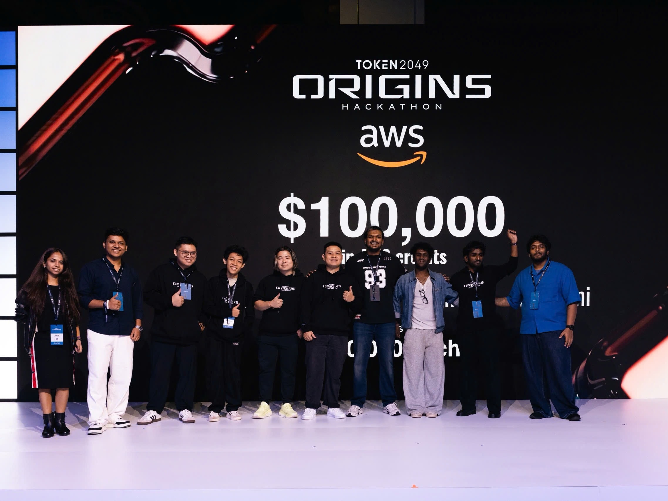 TOKEN2049 Origins Hackathon finalists on stage in front of the AWS prize board
