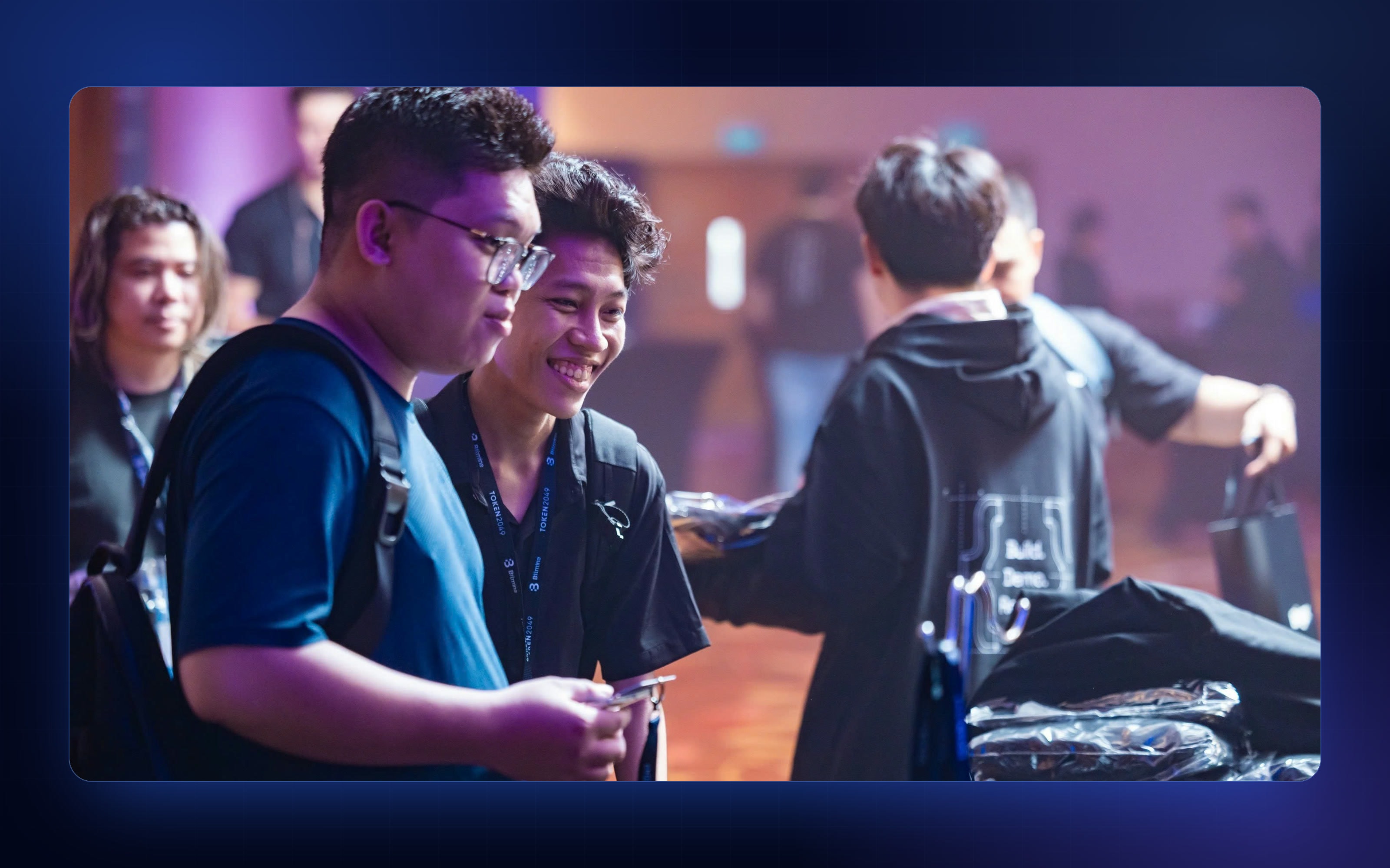 Hackathon participants laughing together at the TOKEN2049 Origins swag table